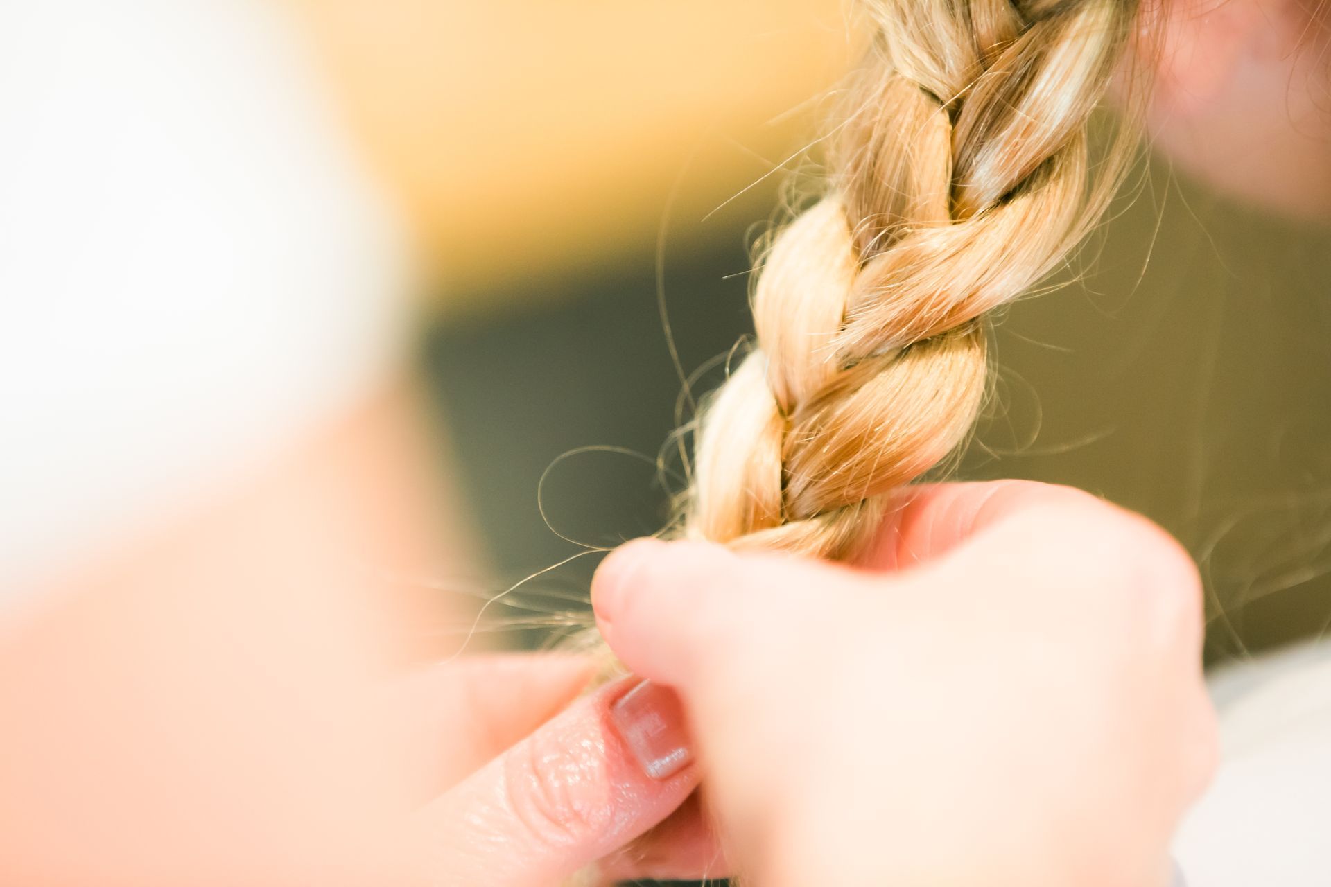 Une coiffeuse réalise une tresse sur une femme blonde