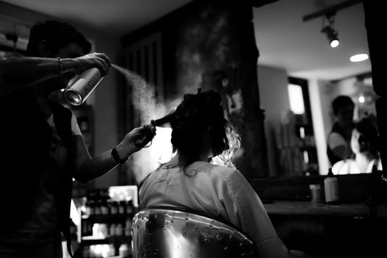 Coiffeur vaporise de la laque sur une chevelure.