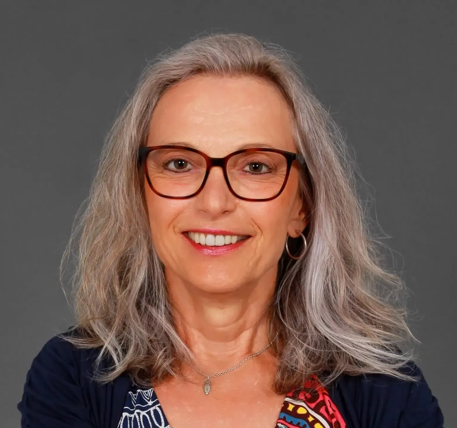 Frau mit grauen Haaren und Brille lächelt in die Kamera.