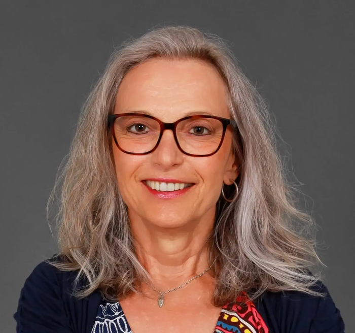 Frau mit grauen Haaren und Brille lächelt in die Kamera.