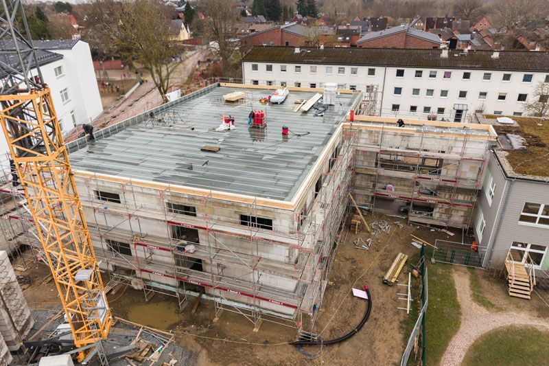 Das rotziegelgedeckte Dach eines Hauses mit abgerundetem Turm und rechteckigen Fenstern hebt sich vom blauen Himmel ab.
