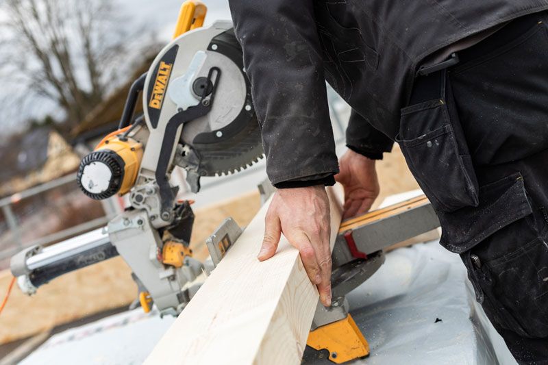 Weißes Gebäude mit rotem Ziegeldach, kleinem Bogenfenster, Büschen und einer Straßenlaterne.