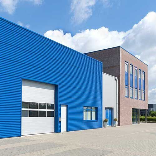 Blaue und gemauerte Industriegebäude mit großem Garagentor und Fenstern vor blauem Himmel.