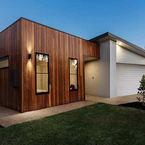 Modernes Haus mit Holzverkleidung, schwarzgerahmten Fenstern und Garage in der Abenddämmerung.