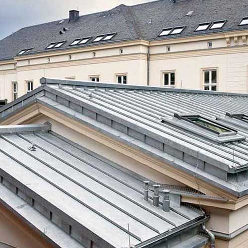 Metalldach eines mehrgeschossigen Gebäudes mit Fenstern und Oberlichtern. Farbpalette in Grau- und Beigetönen.