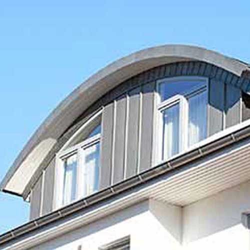 Gebogenes Metalldach mit vertikalen Paneelen, Fenstern und klarem blauen Himmel.