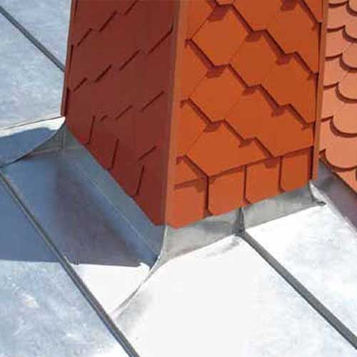 Nahaufnahme eines Schornsteins und der Dacheindeckung. Der Schornstein ist orange, das Dach silberfarben und die Eindeckung aus Metall.