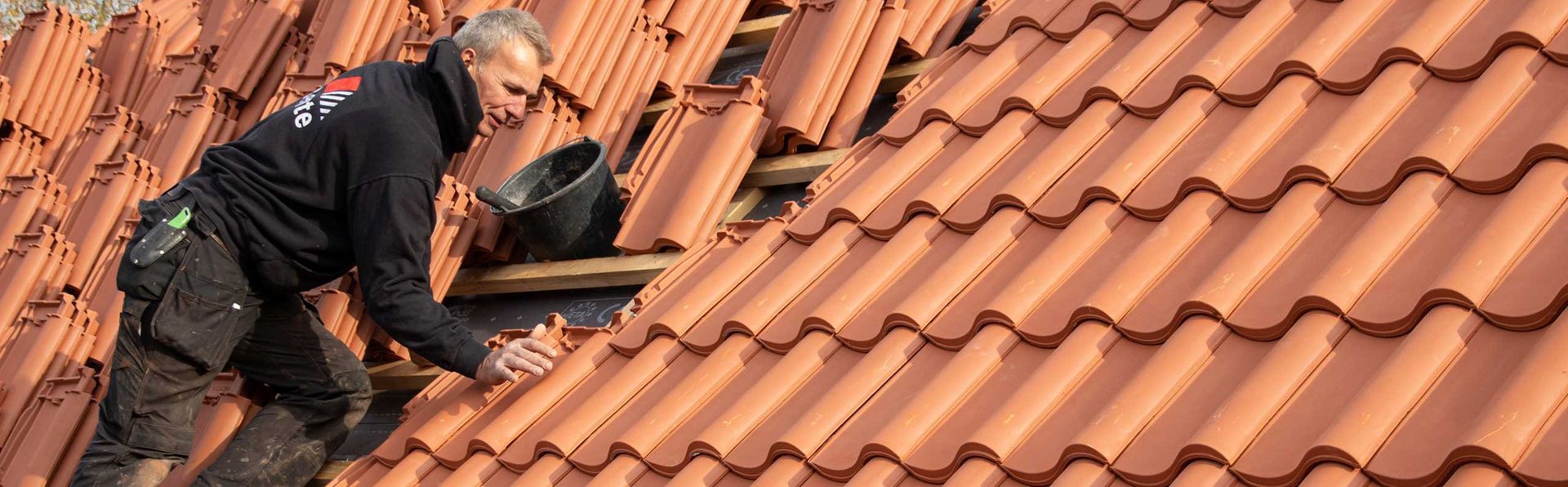 Eine Person arbeitet an einem mit Terrakotta-Ziegeln gedeckten Dach. Sie überprüft oder verlegt Ziegel.