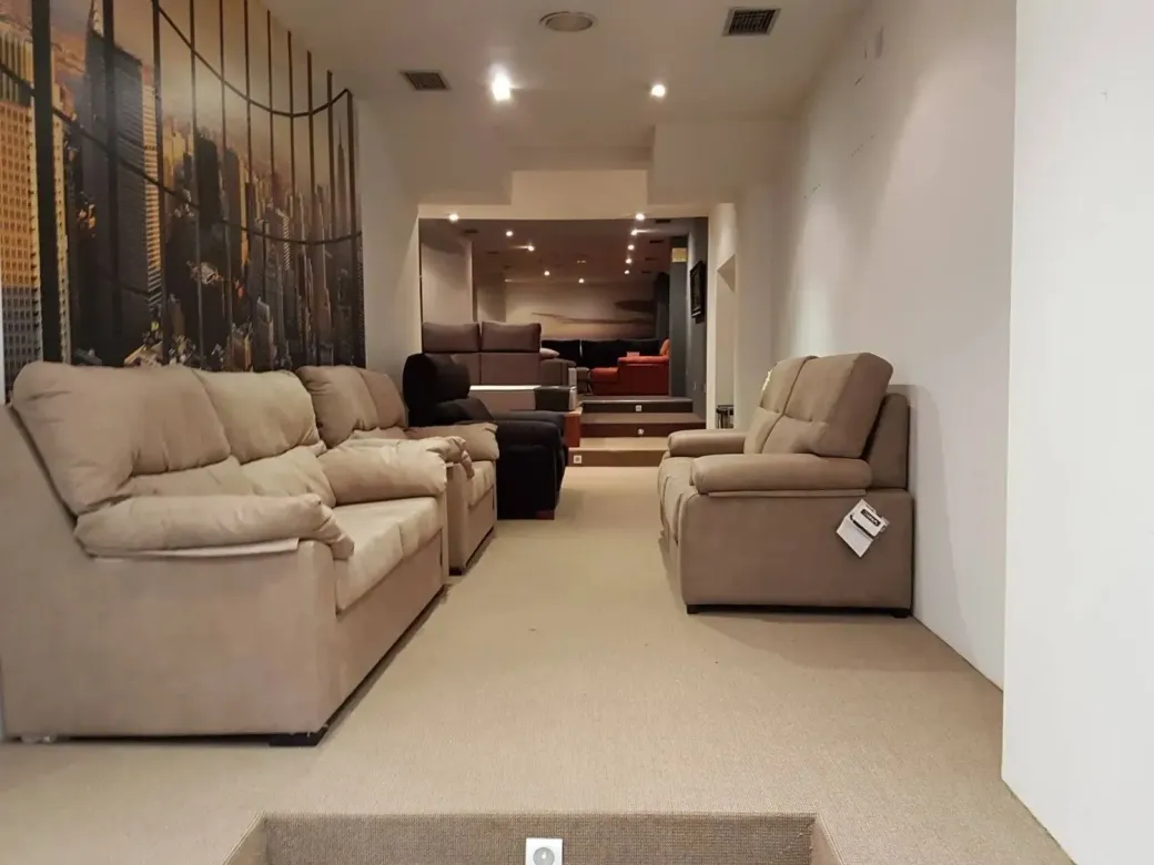 En el escaparate de una tienda de muebles se pueden ver sofás y sillones de color marrón claro dispuestos sobre una moqueta.