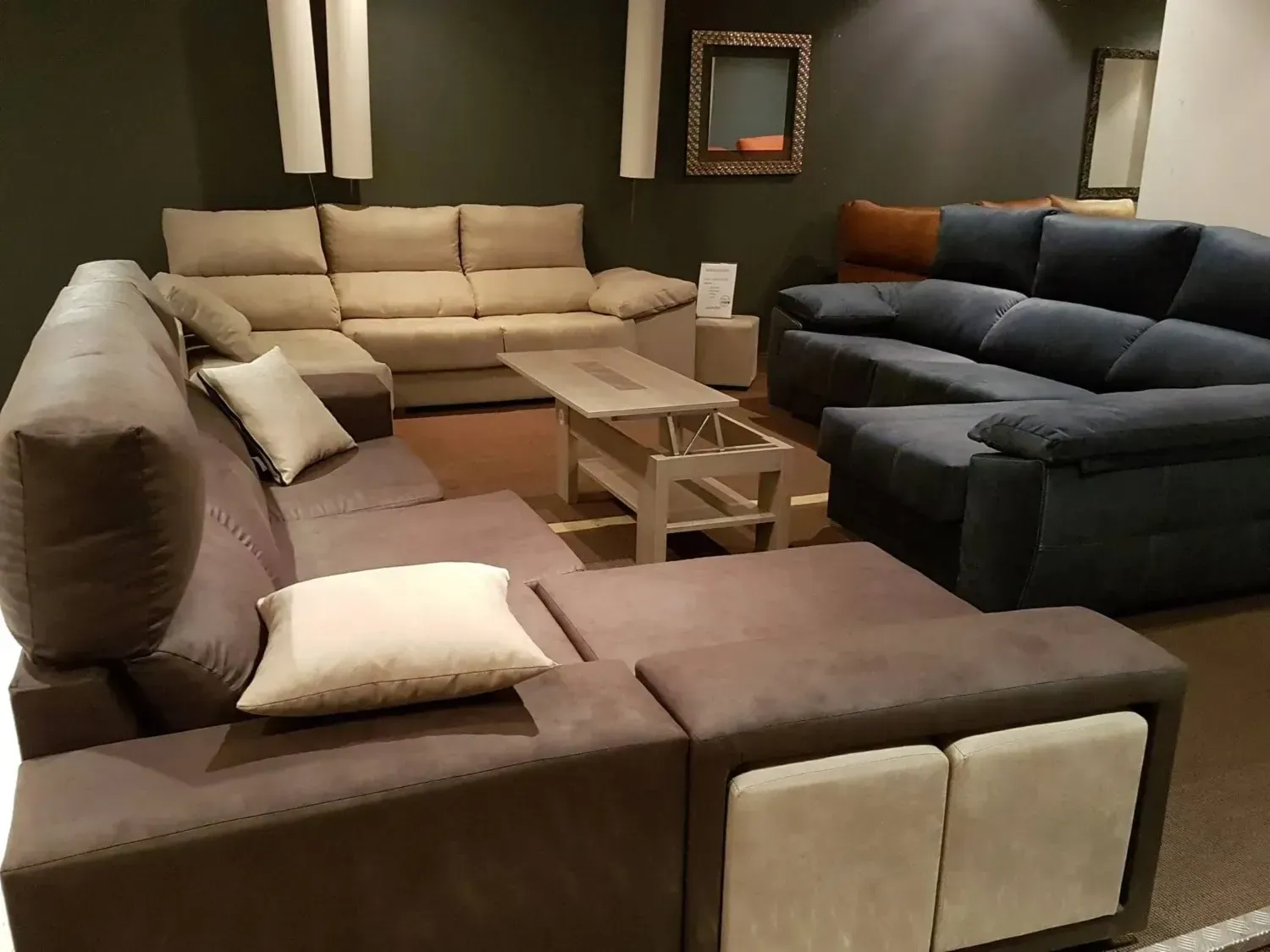 En la sala de exposición se muestran tres sofás modulares en color beige claro, marrón oscuro y azul marino.