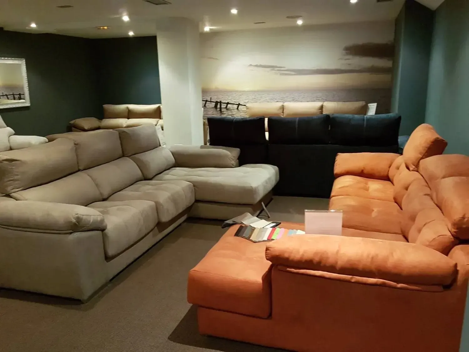 Sala de exposición de muebles con tres sofás modulares en color beige, gris oscuro y naranja.