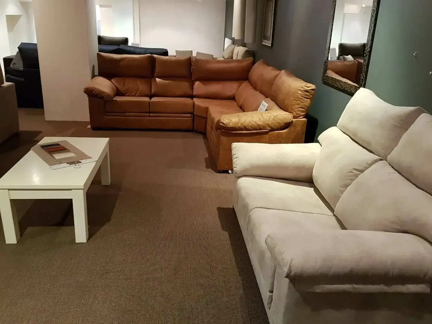 Una sala de exposición de muebles que muestra un sofá de dos plazas de color claro, un sofá esquinero modular.