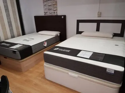 En una sala de exposición con suelo de madera, se muestran dos camas con colchones.