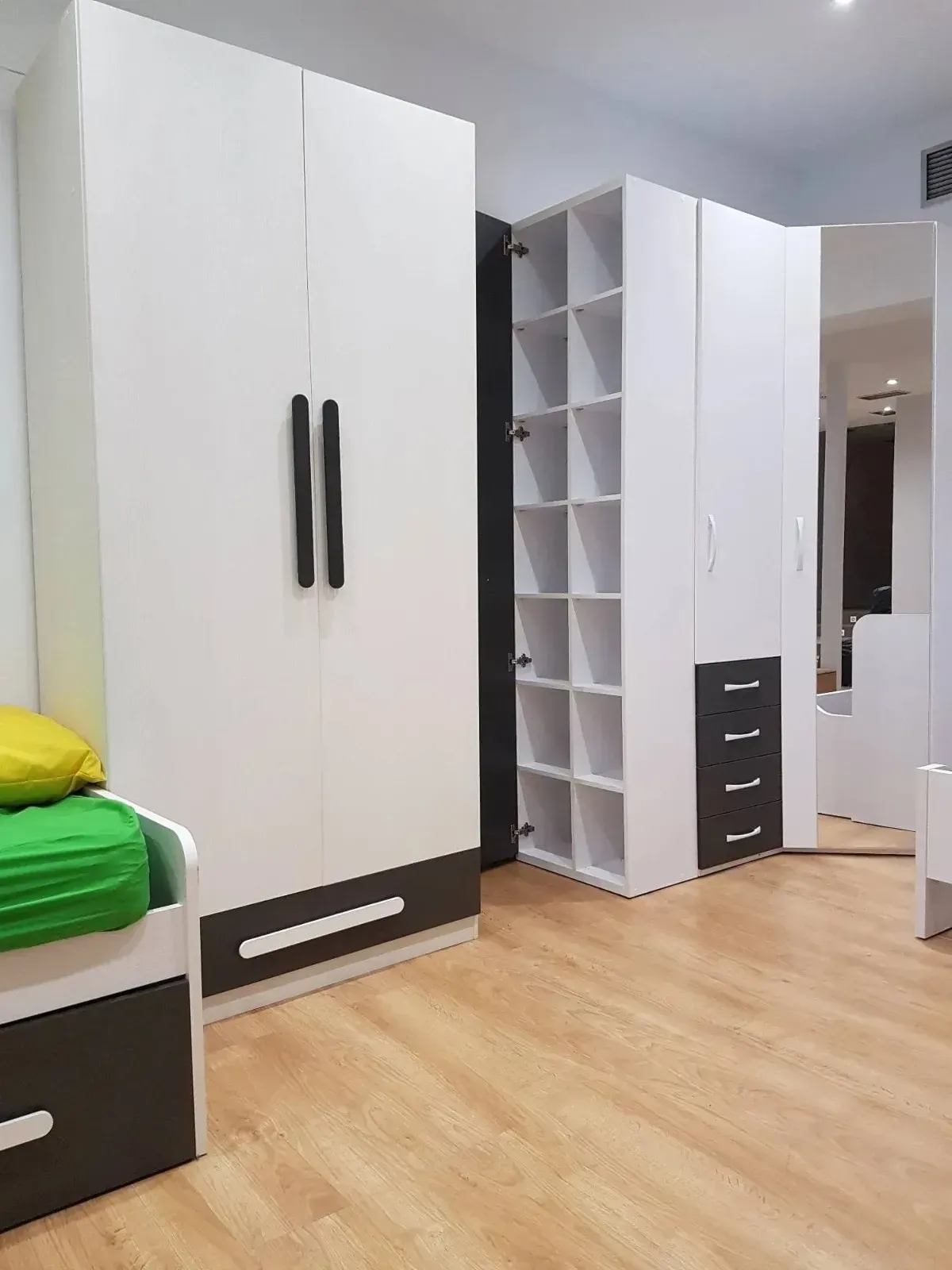 Un dormitorio con dos armarios modernos, uno blanco y otro gris oscuro, uno de ellos con estantes abiertos.