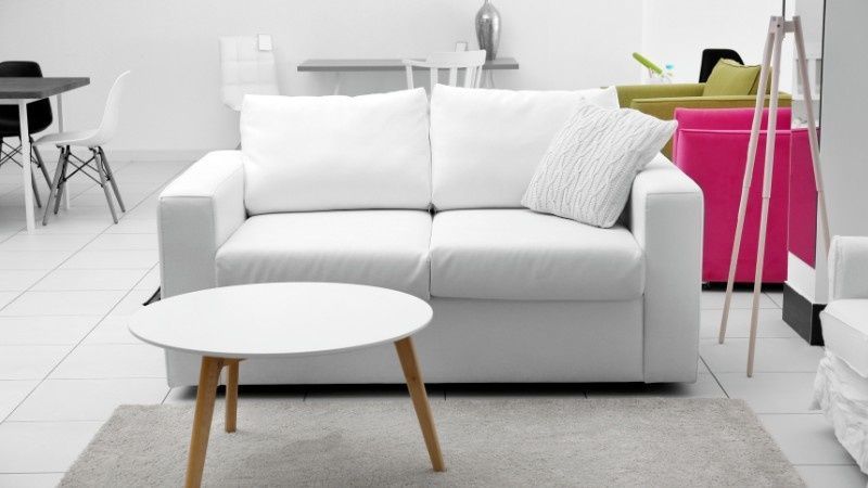 Una habitación moderna con un sofá blanco, una mesa de centro redonda con patas de madera y sillas coloridas al fondo.