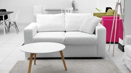 Una habitación moderna con un sofá blanco, una mesa de centro redonda con patas de madera y sillas coloridas al fondo.