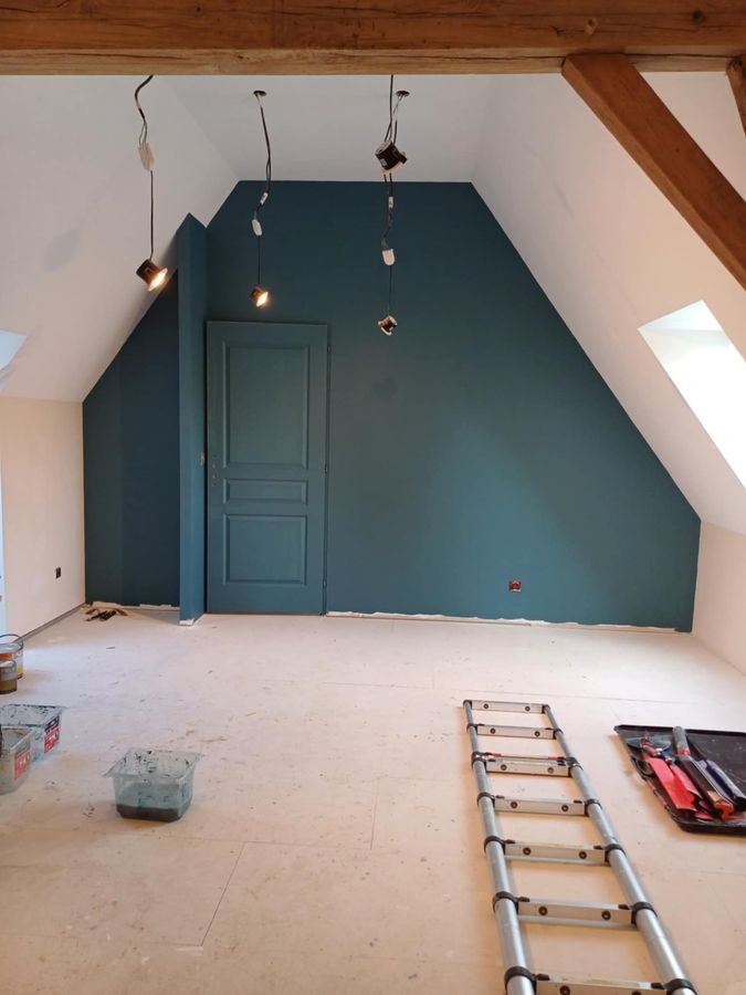 Pièce en cours de peinture, murs blancs, rouleau de peinture à gauche, échelle, fenêtres, meubles recouverts de plastique.