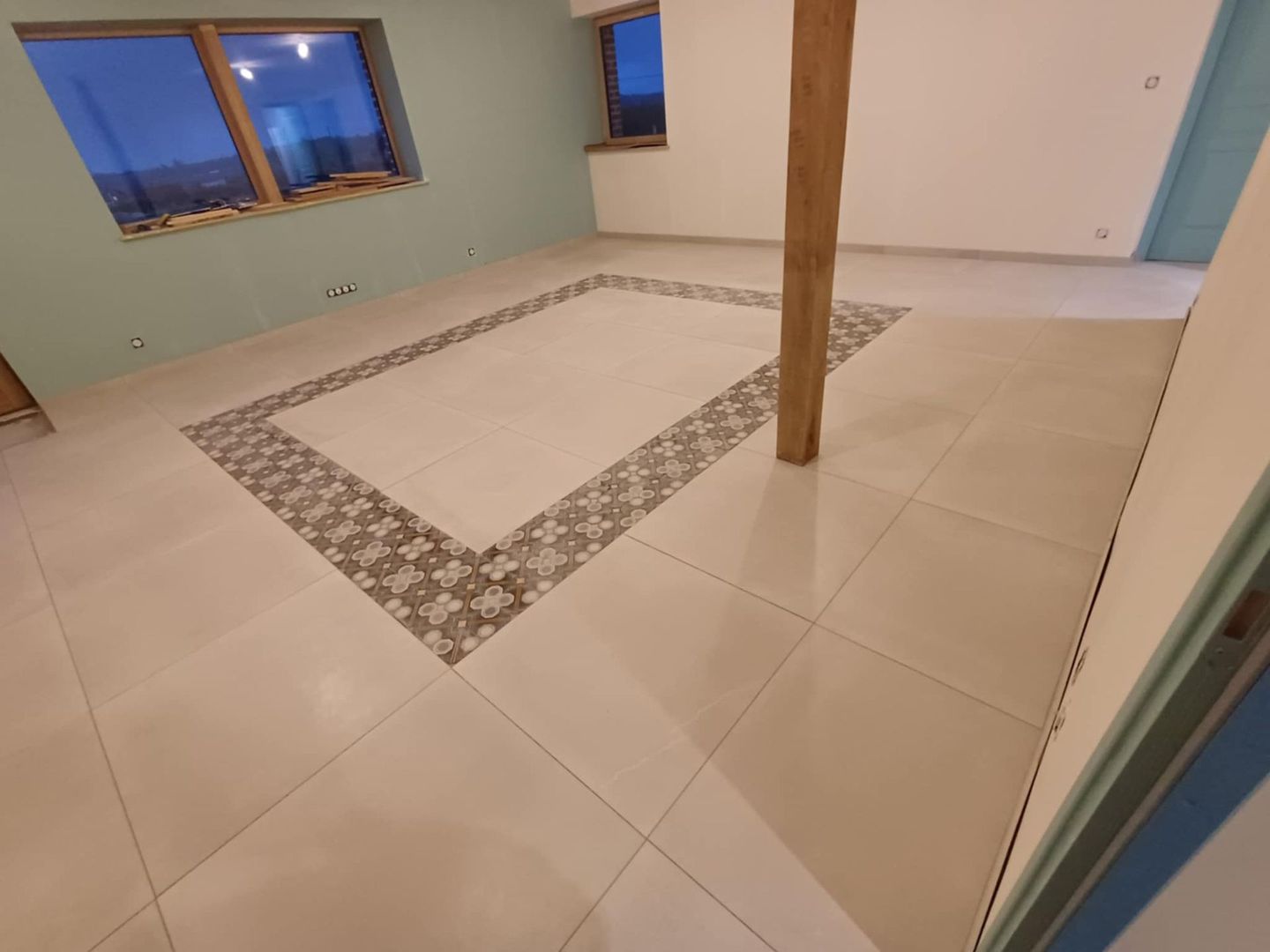 Une personne portant des gants est à genoux et installe des carreaux de couleur foncée sur le sol.