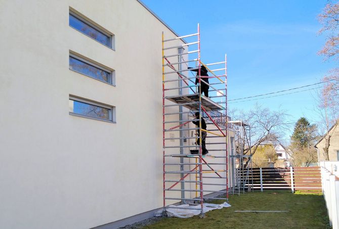 Personne sur un échafaudage peignant l'extérieur blanc d'un bâtiment sous un ciel bleu.