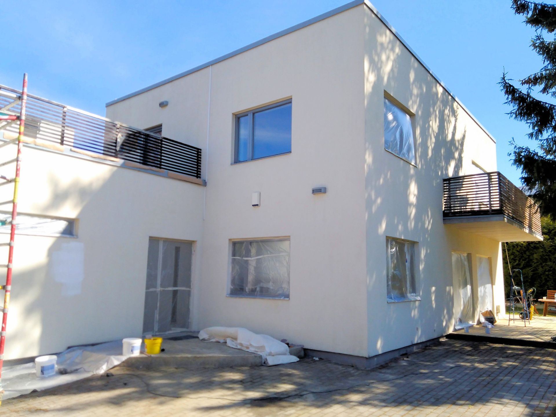 Bâtiment moderne de deux étages avec murs beiges, balcons et fenêtres, matériaux de construction au sol, ciel bleu.