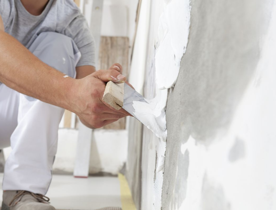 Personne appliquant du plâtre sur un mur blanc avec une truelle.
