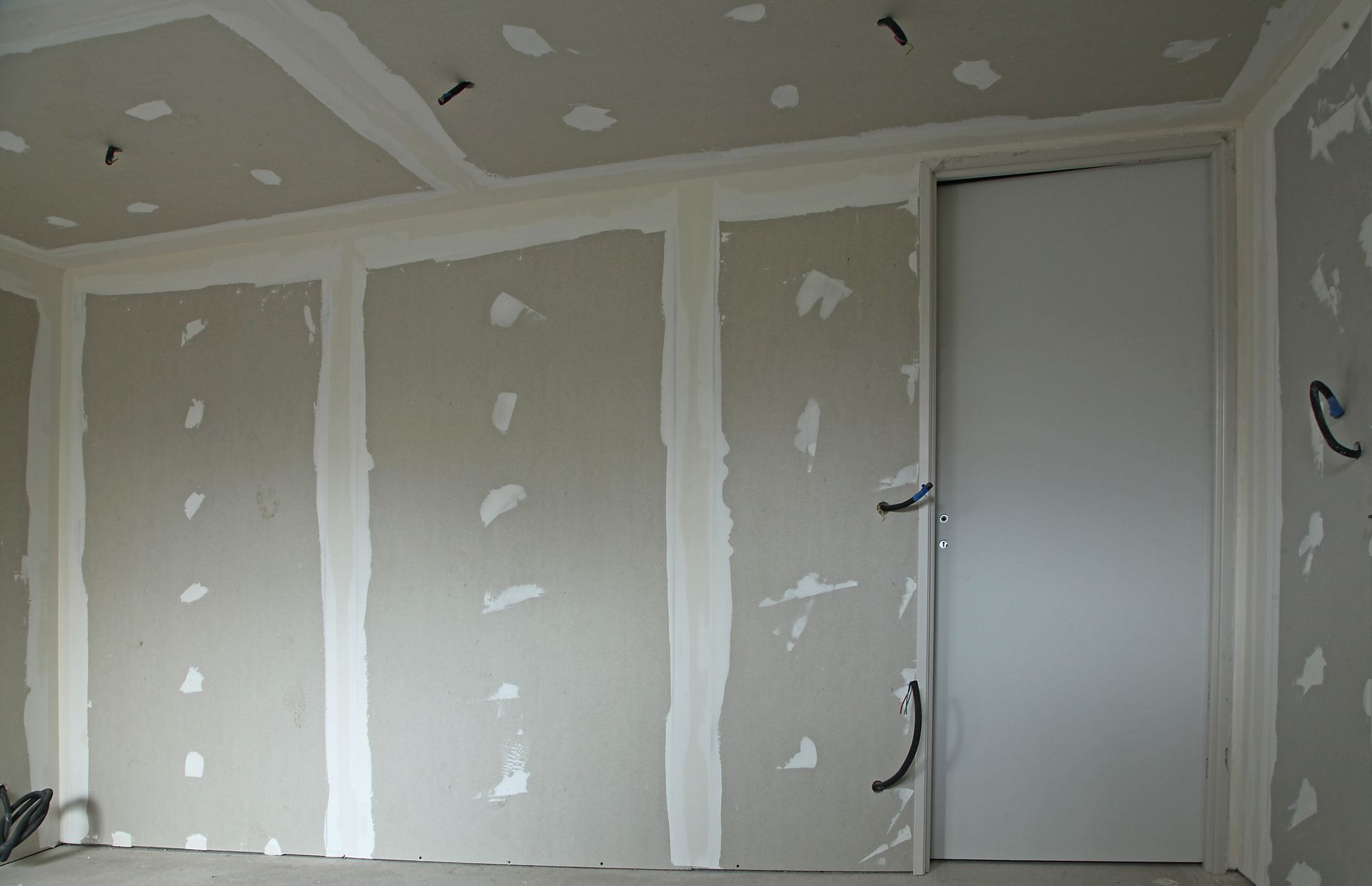 Pièce intérieure avec cloisons sèches; joints non finis, porte et fils électriques visibles.