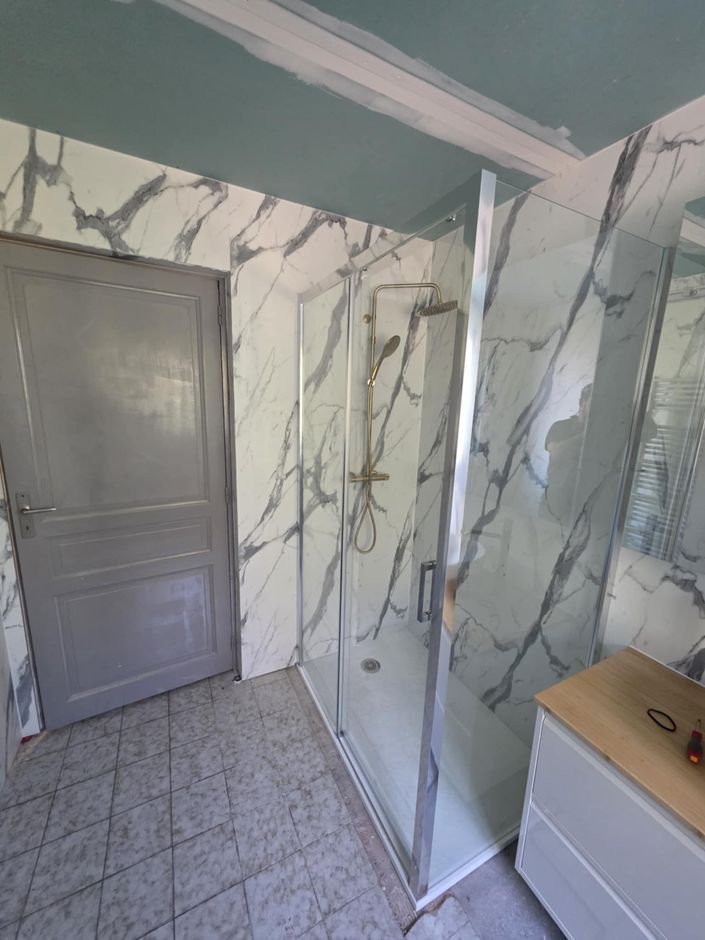 Salle de bains blanche moderne avec douche en verre, miroir et porte-serviettes.