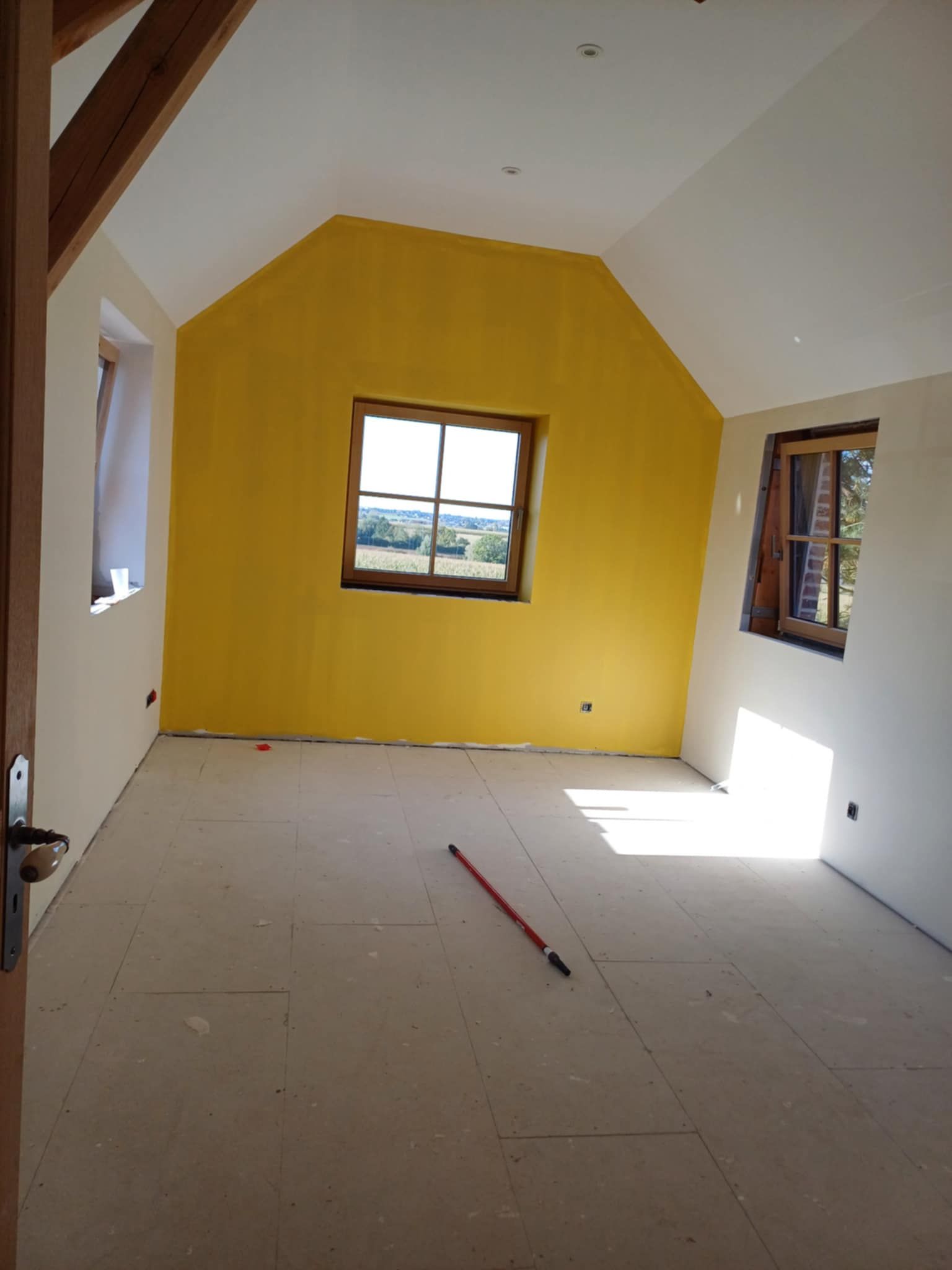 Intérieur d'une chambre mansardée avec poutres en bois apparentes et porte ouverte.