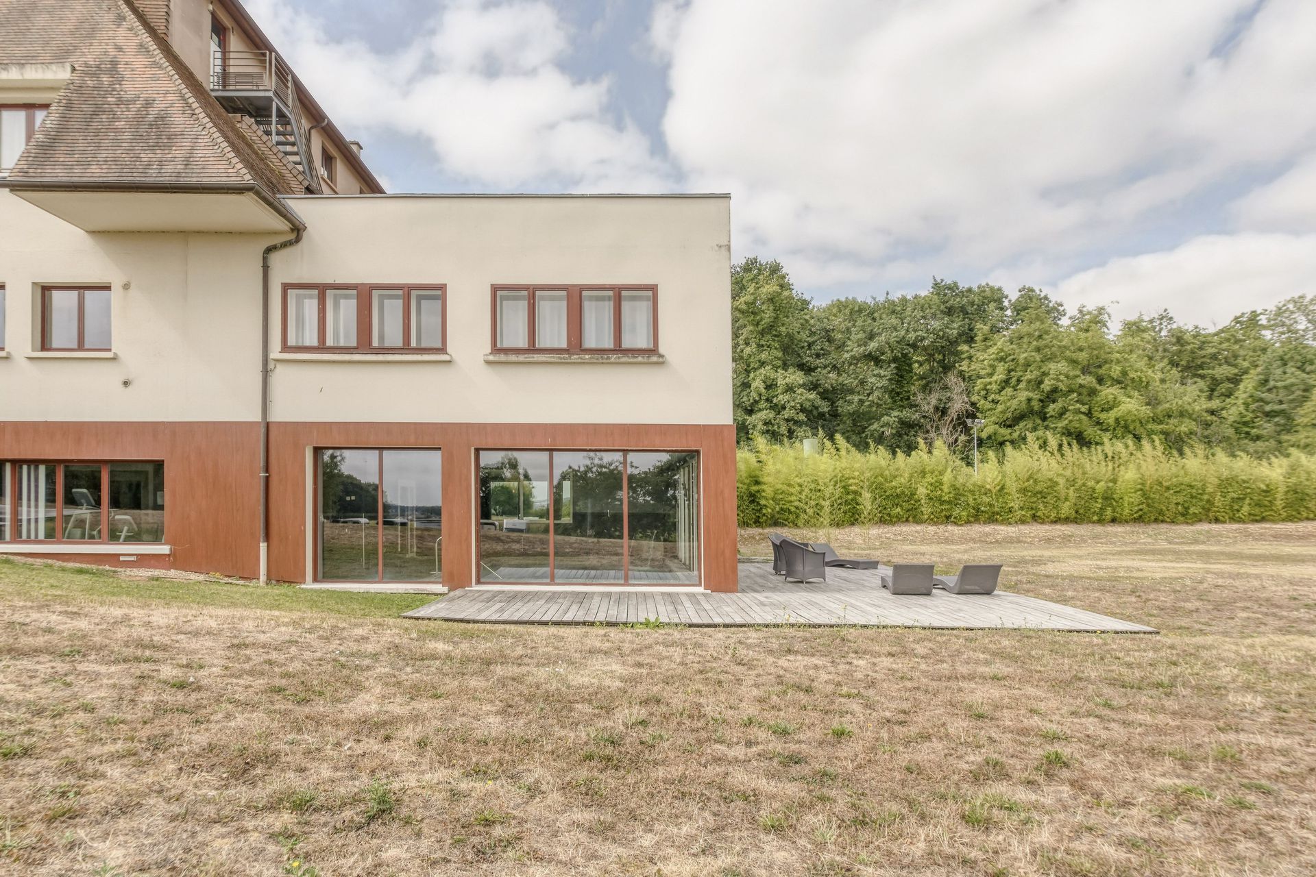 Établissement beige et marron avec une terrasse, un salon de jardin et un terrain herbu