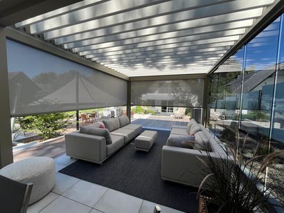Terrasse mit grauem Sofa, Sonnenschirmen und Pergola. Rechts eine Glaswand, im Hintergrund der Garten.