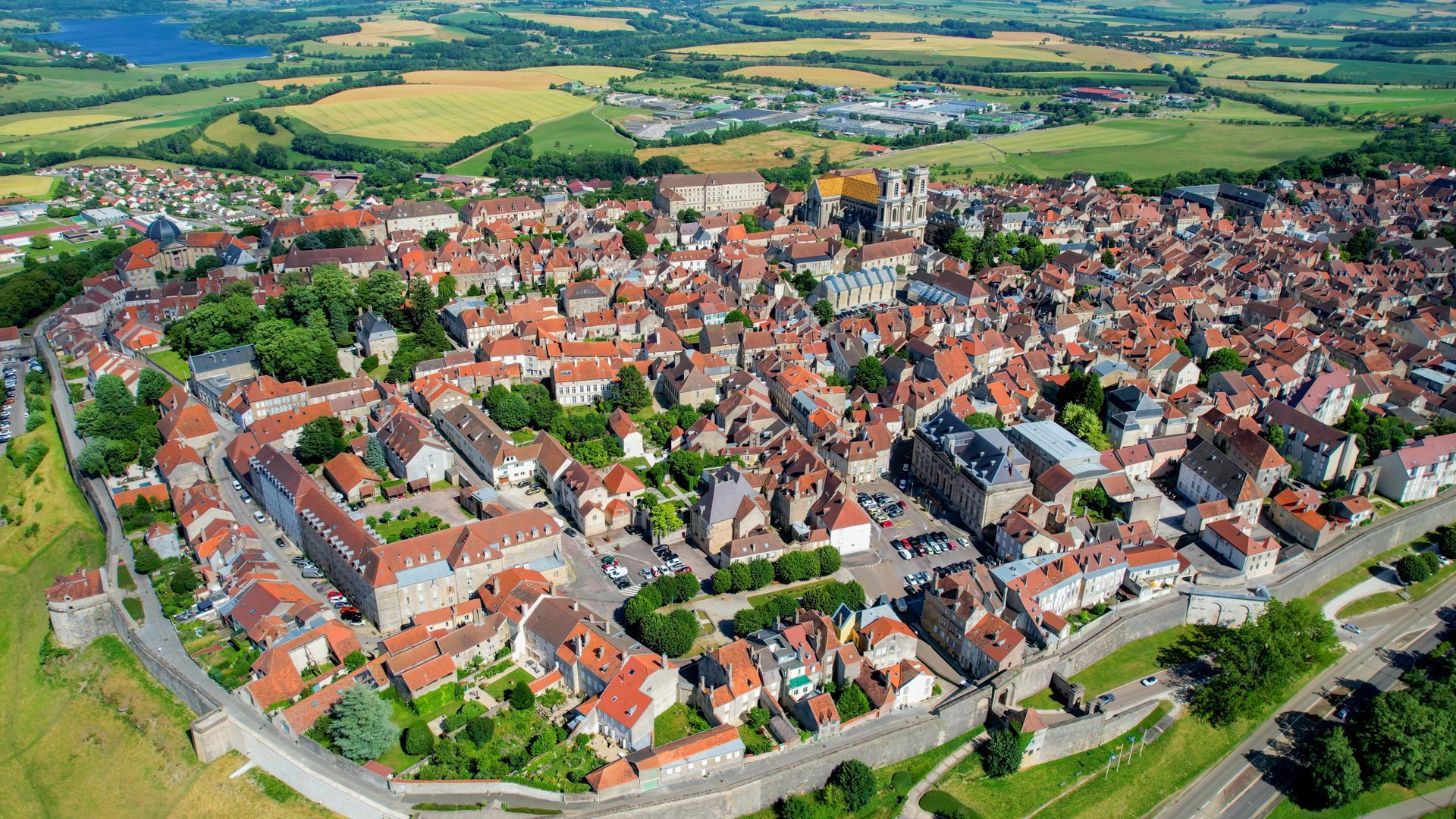 Vue aérienne d'un village dense avec des maisons aux toits rouges, une église et des champs verdoyants environnants