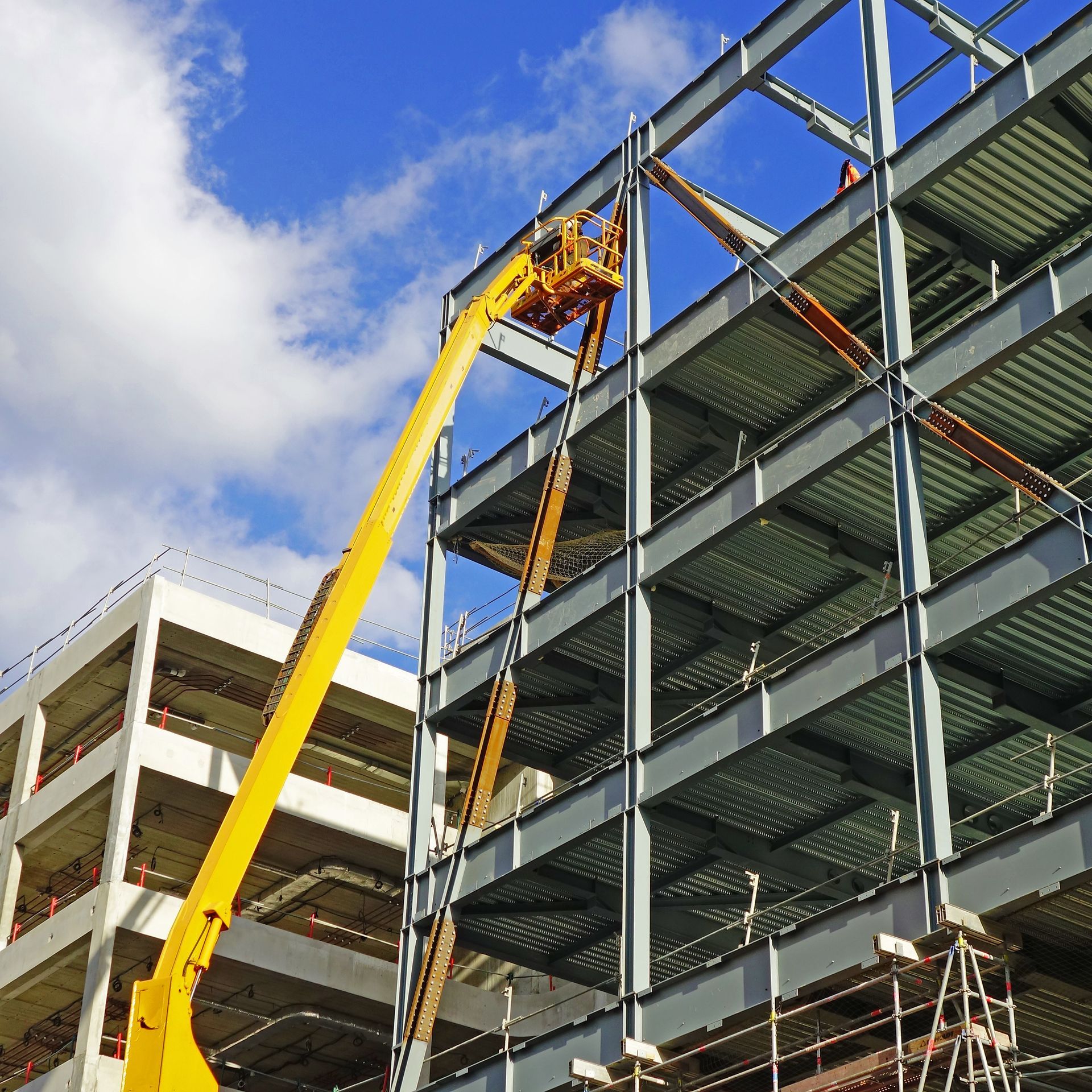Ascenseur de chantier jaune à côté d'une structure métallique sous un ciel bleu