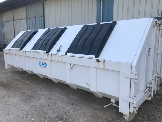Conteneur à déchets industriel blanc avec des grilles d'aération noires à côté d'un bâtiment métallique sur du gravier.