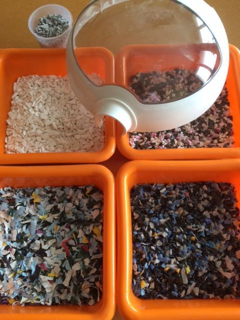 Des bacs de rangement orange remplis de petits morceaux et granulés de plastique, avec une loupe au-dessus.