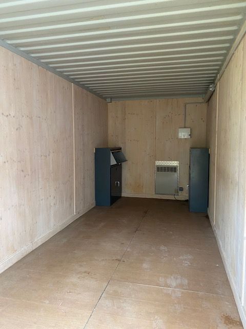 Intérieur d'un conteneur cargo vide avec parois en contreplaqué, plafond en métal et deux armoires bleues au fond.