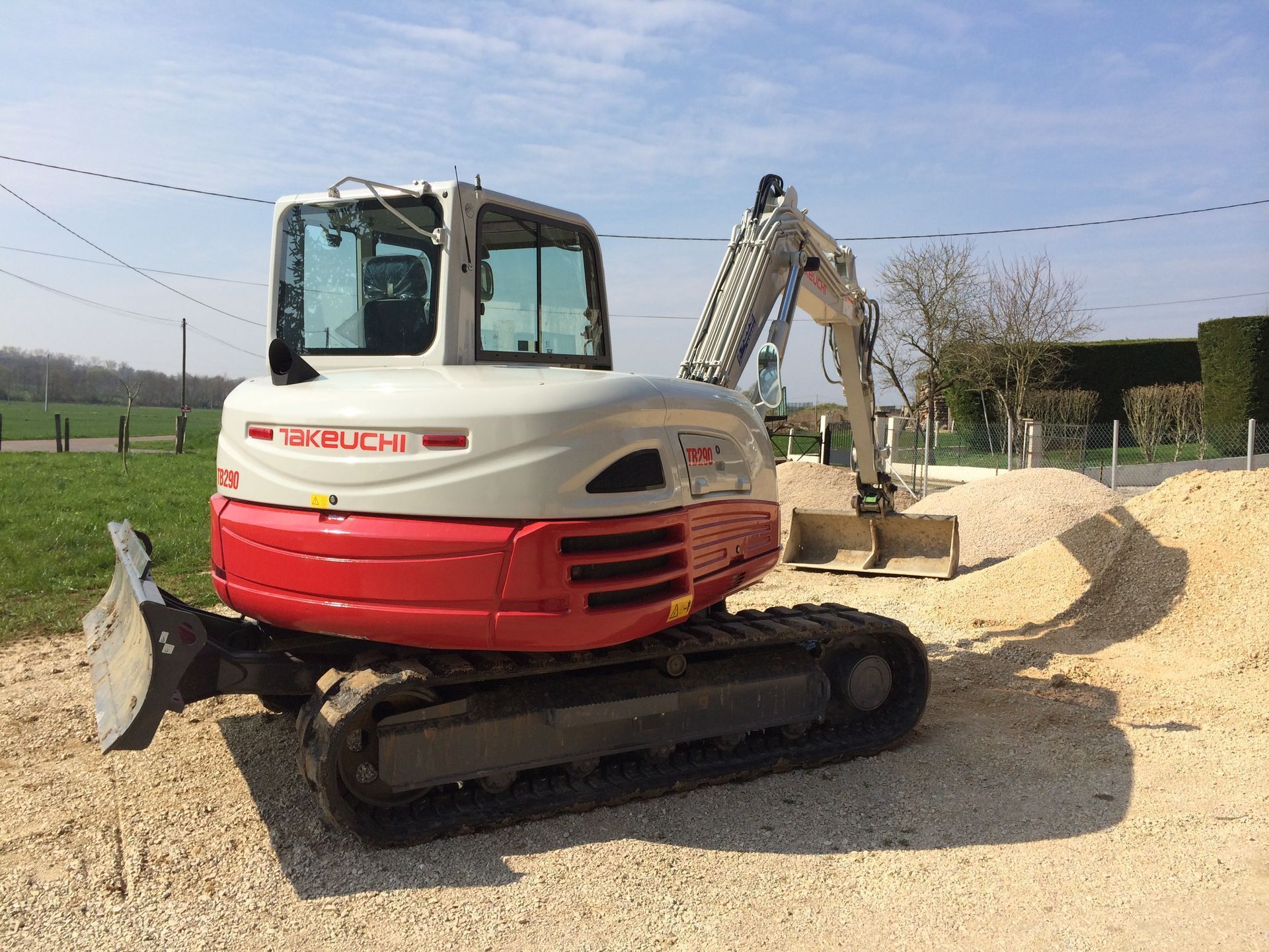 Une pelleteuse rouge et blanche sur chenilles, à côté d'un tas de sable sur un chantier de construction.