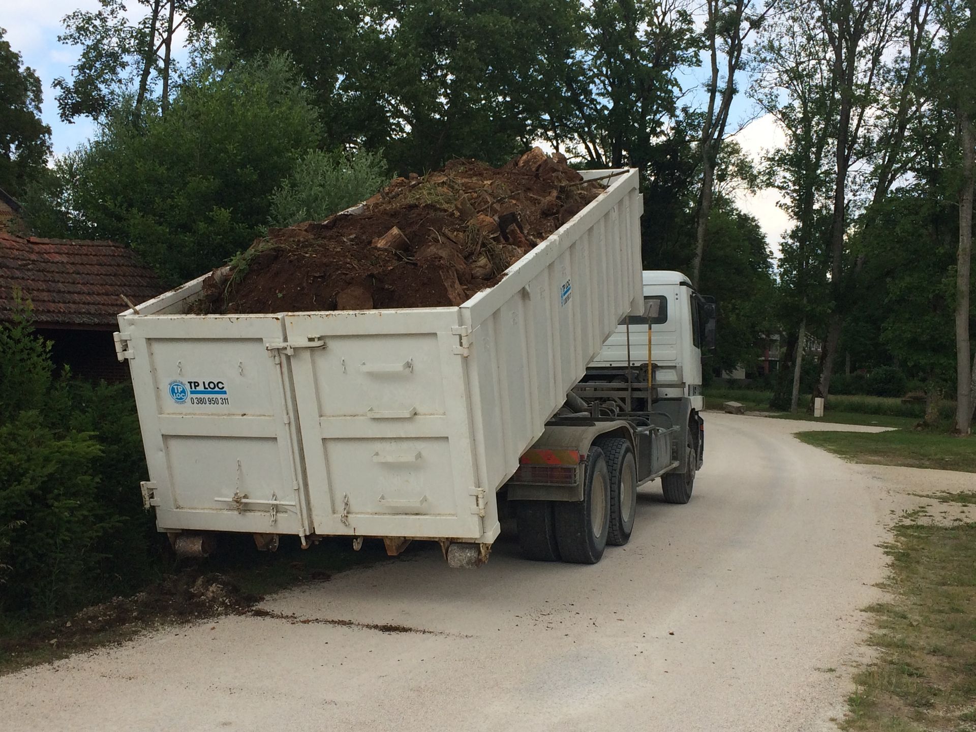 Un camion-benne blanc chargé de terre sur une route de campagne sinueuse