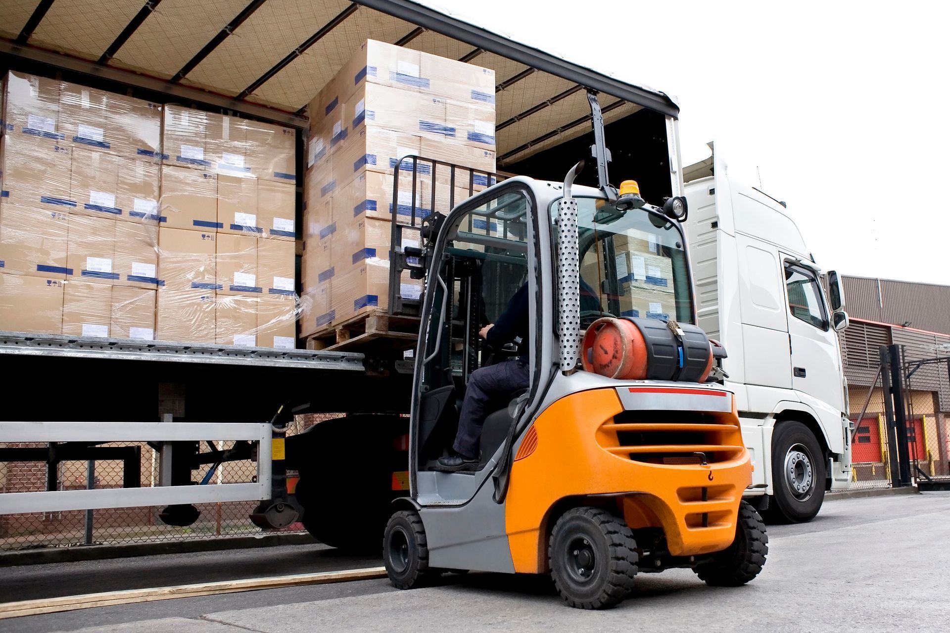 Un chariot élévateur orange charge des cartons empilés sur un camion au quai de l'entrepôt