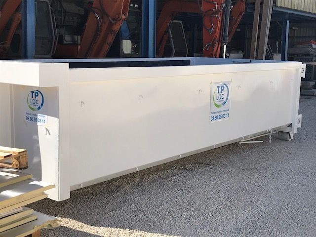 Trémie industrielle blanche posée sur du gravier à côté de machines rouges, avec des autocollants portant le logo TP.