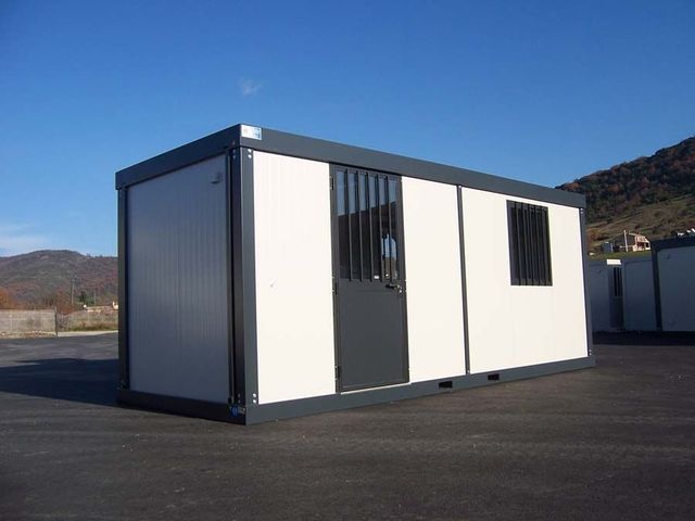 Bâtiment modulaire portable avec panneaux blancs et finitions foncées sur un terrain pavé extérieur