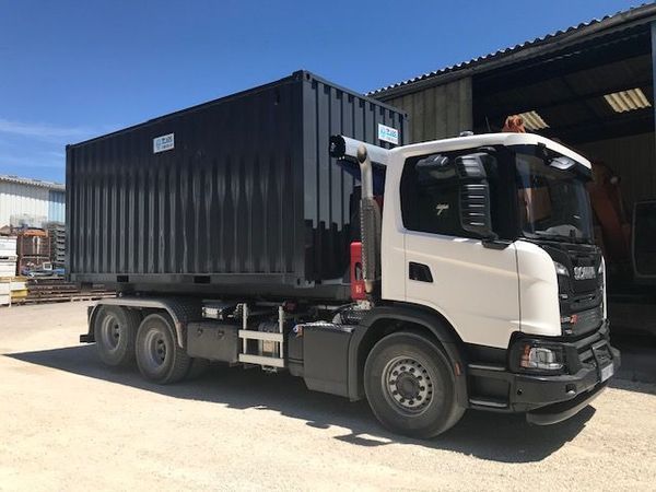 Camion blanc transportant un conteneur noir dans une zone industrielle