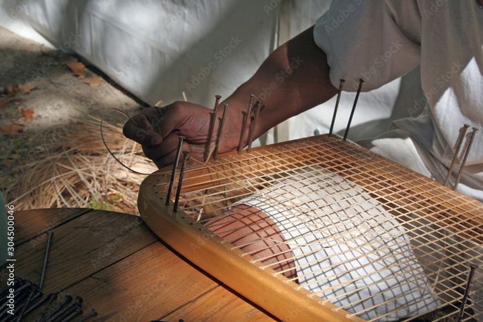 Une personne travaille sur une chaise en osier avec des clous.