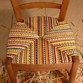 Une chaise en bois avec un siège coloré est assise sur un tas de foin.