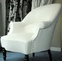 Une chaise blanche est assise dans une pièce à côté d'une fenêtre.