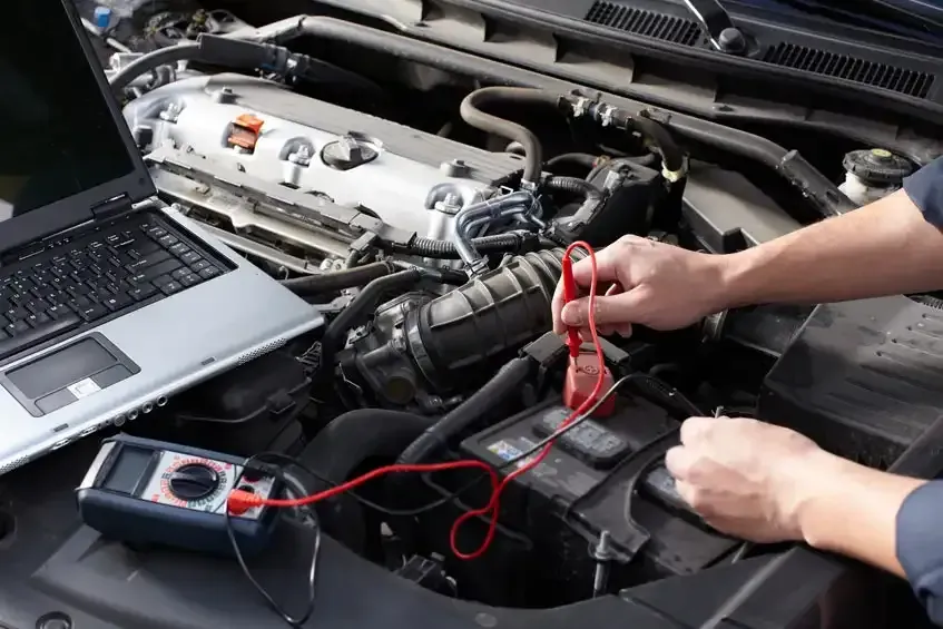 Una persona está trabajando en el motor de un automóvil con una computadora portátil.