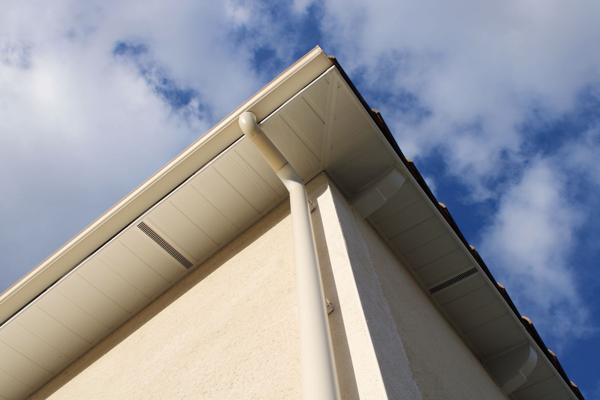 Coin d'un bâtiment beige, la toiture se détachant sur un ciel bleu nuageux.