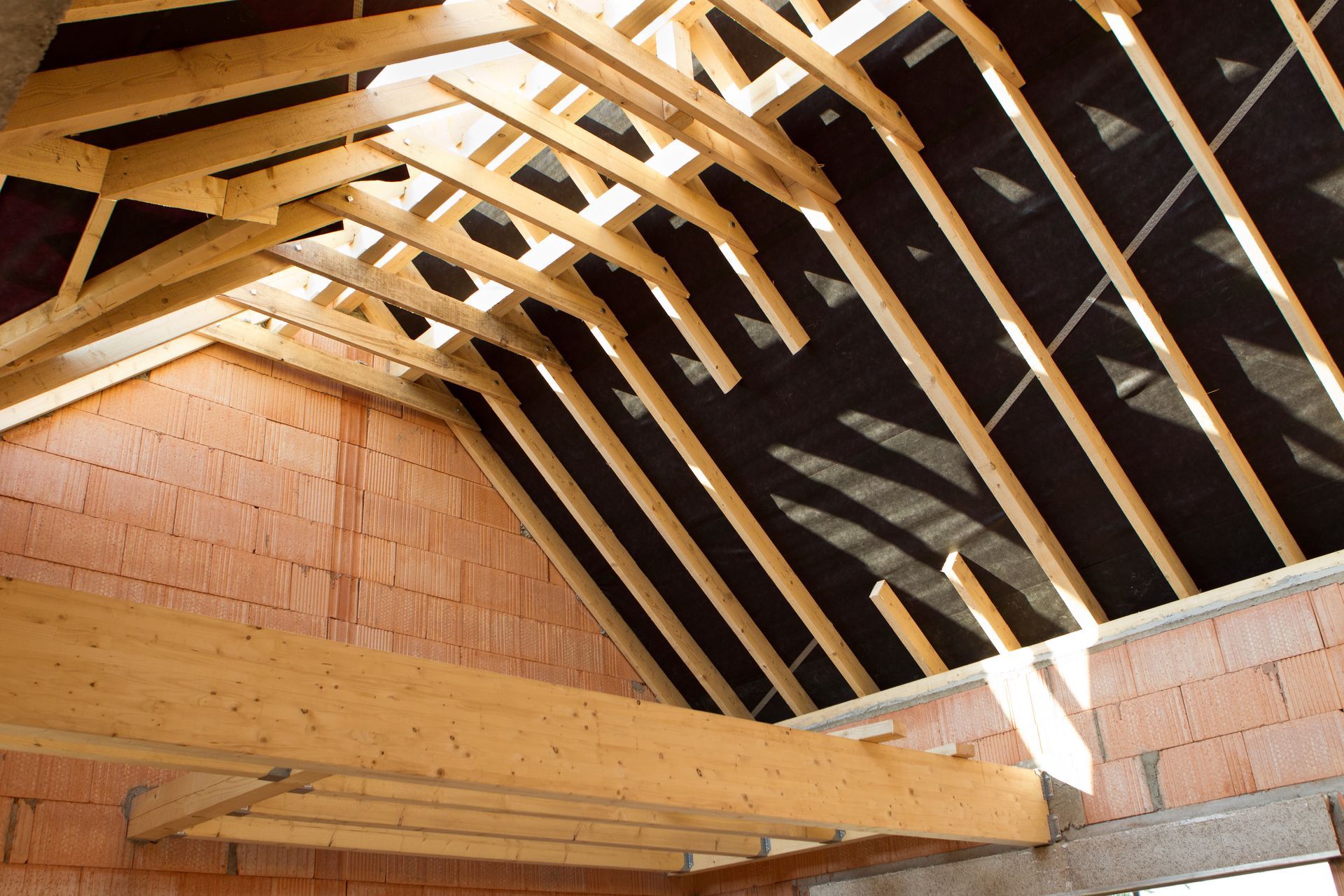 Charpente apparente en bois et murs en briques roses à l'intérieur d'un bâtiment inachevé