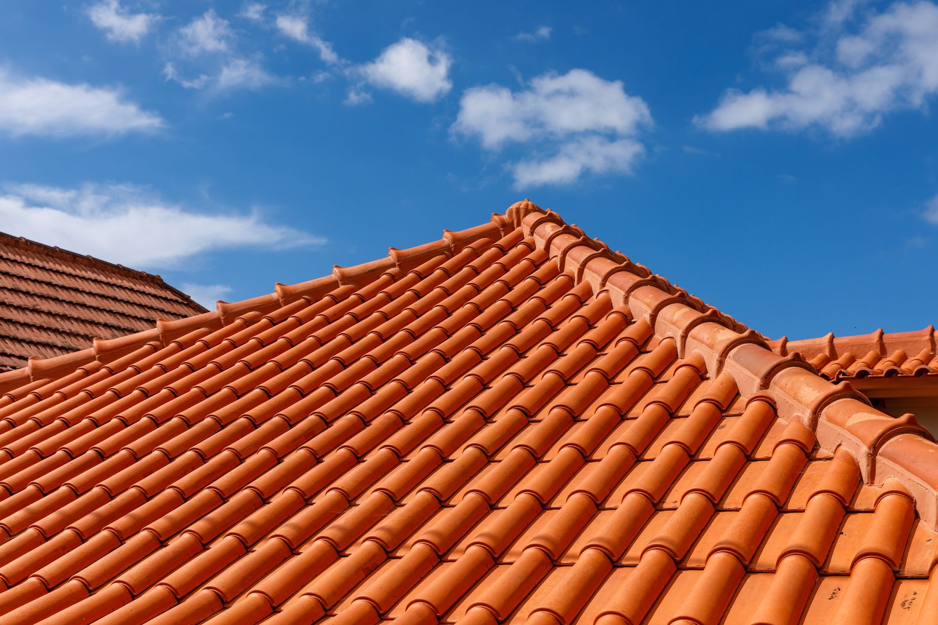 Toit de tuiles en terre cuite orange sous un ciel bleu éclatant parsemé de nuages.
