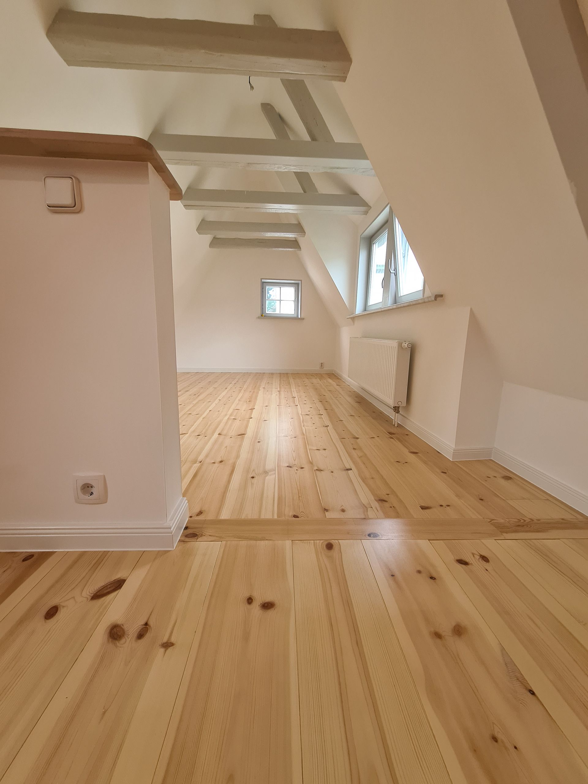 ein leerer Raum mit einem Holzboden und weißen Wänden .