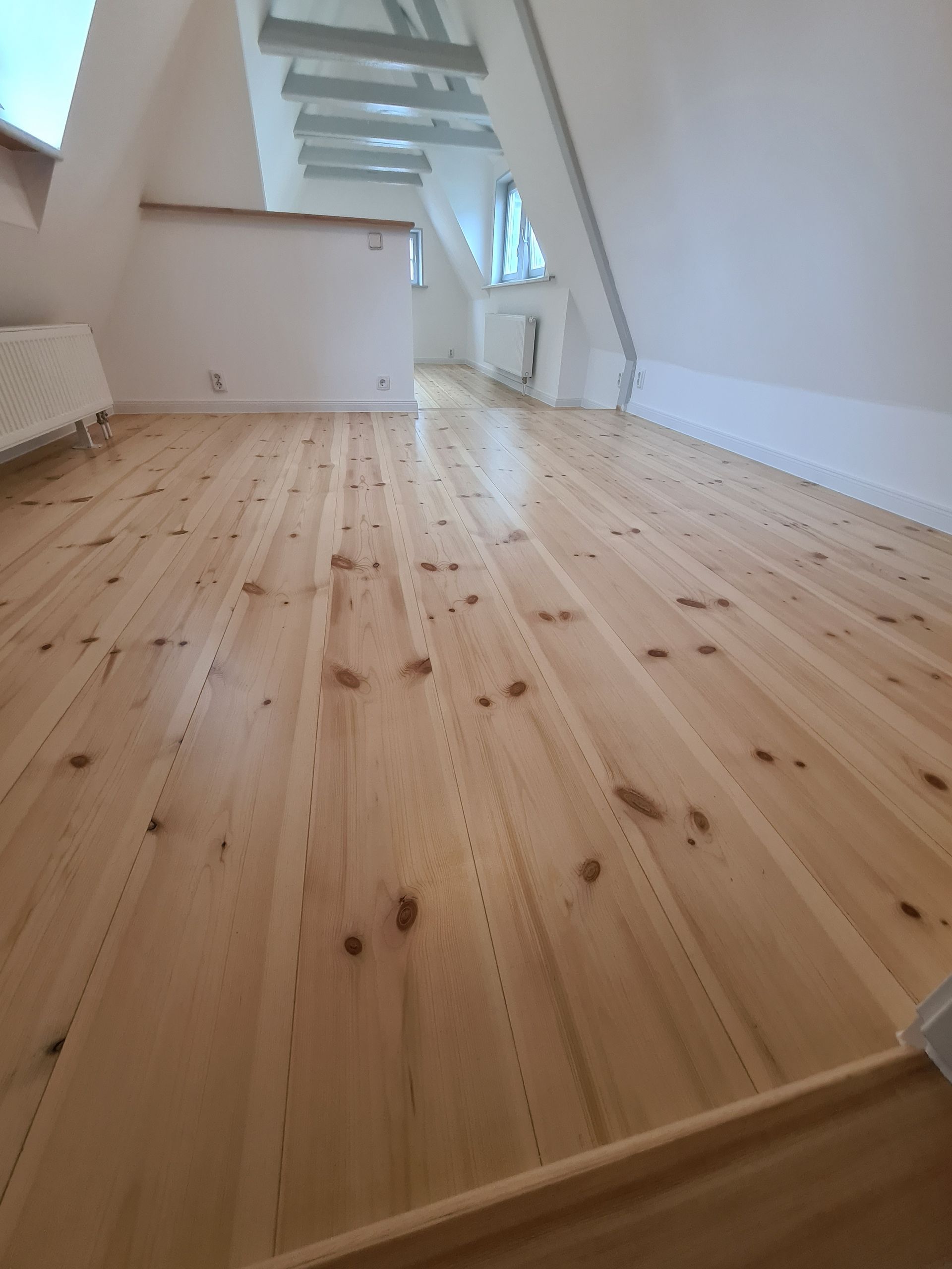 ein leerer Raum mit einem Holzboden und weißen Wänden .